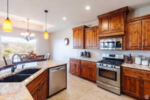 Kitchen with appliances with stainless steel finishes, brown cabinetry, backsplash, hanging light fixtures, and a chandelier