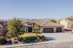 Mediterranean / spanish-style house featuring stone siding, a front yard, a garage, driveway, and stucco siding