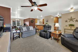 Living room with light carpet, a chandelier, ceiling fan, crown molding, and a glass covered fireplace