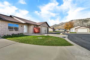 Single story home with brick siding, a front lawn, a shingled roof, driveway, and a mountain view