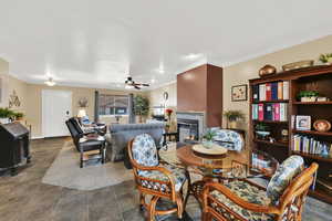 Dining area featuring ornamental molding, a multi sided fireplace, a ceiling fan, and dark tile patterned floors
