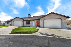 Ranch-style house with driveway, brick siding, a front lawn, a chimney, and an attached garage