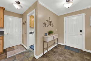 Entryway with washer / dryer, crown molding, and dark stone finish flooring