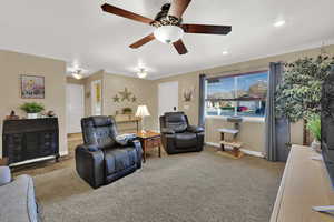 Living room featuring crown molding, ceiling fan, and carpet floors