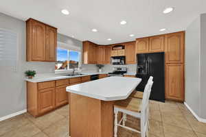 Kitchen with a kitchen bar, black appliances, brown cabinets, a kitchen island, and recessed lighting