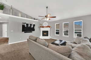 Living room with carpet, a glass covered fireplace, ceiling fan, and lofted ceiling