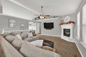 Living room with a glass covered fireplace, vaulted ceiling, carpet flooring, a ceiling fan, and arched walkways