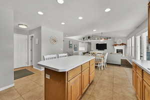 Kitchen with brown cabinets, a center island, light tile patterned floors, a warm lit fireplace, and light countertops