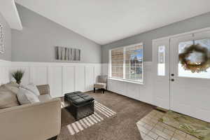 Foyer featuring a wainscoted wall, a decorative wall, lofted ceiling, light tile patterned flooring, and light colored carpet