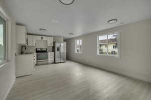 Kitchen with white cabinetry, light countertops, appliances with stainless steel finishes, light wood finished floors, and open floor plan