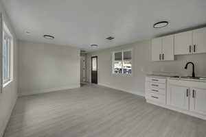 Kitchen featuring white cabinets, light wood-type flooring, and light stone countertops