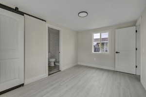 Unfurnished bedroom with a barn door, light wood-style floors, and ensuite bath