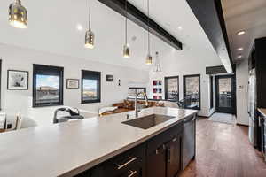 Kitchen with dark cabinetry, hanging light fixtures, open floor plan, dark wood-style flooring, and beam ceiling