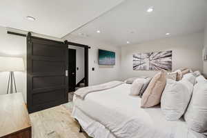 Bedroom with a barn door, light wood finished floors, and recessed lighting
