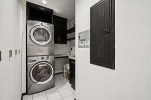 Washroom with electric panel, stacked washer / drying machine, light tile patterned flooring, and cabinet space