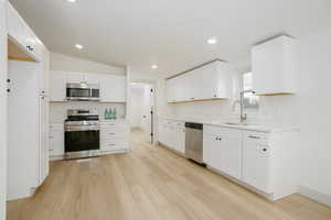 Kitchen with appliances with stainless steel finishes, light wood-style flooring, white cabinets, lofted ceiling, and recessed lighting