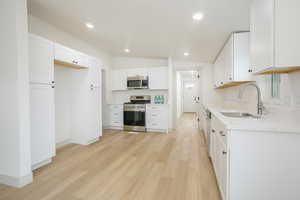 Kitchen with light wood-style floors, appliances with stainless steel finishes, vaulted ceiling, white cabinetry, and light stone countertops