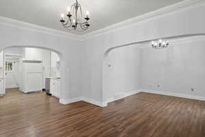 Unfurnished dining area featuring a chandelier, ornamental molding, and dark wood finished floors