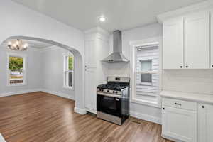 Kitchen with backsplash, gas range, white cabinetry, wall chimney exhaust hood, and arched walkways