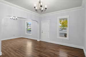 Empty room with a chandelier, crown molding, dark wood-style floors, and arched walkways