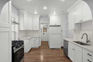 Kitchen featuring appliances with stainless steel finishes, white cabinetry, light stone counters, dark wood finished floors, and tasteful backsplash