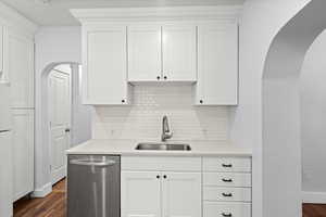 Kitchen featuring arched walkways, white cabinetry, stainless steel dishwasher, dark wood-style floors, and light stone countertops