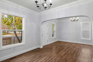 Unfurnished dining area featuring a chandelier, ornamental molding, dark wood-style flooring, and arched walkways