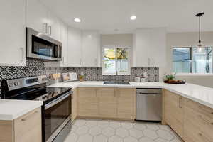 Kitchen featuring stainless appliances, tiled backsplash, modern cabinetry, & pendant lighting