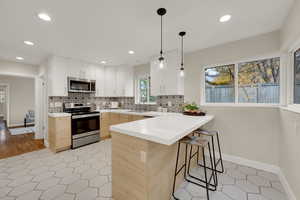 Kitchen with tiled backsplash, a breakfast bar area, appliances with stainless steel finishes, and recessed/pendant lighting