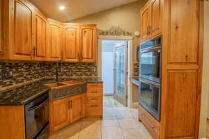 Kitchen with vaulted ceiling, black appliances, light tile patterned flooring, dark stone countertops, and backsplash