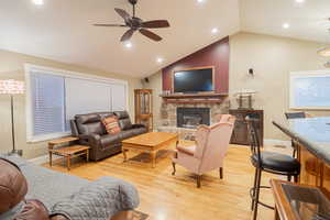 Living room with vaulted ceiling, a stone fireplace, a ceiling fan, light wood-type flooring, and recessed lighting