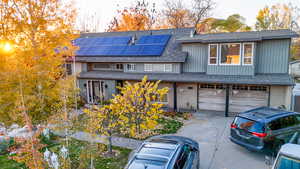 View of front of house featuring brick siding, solar panels, roof with shingles, and driveway