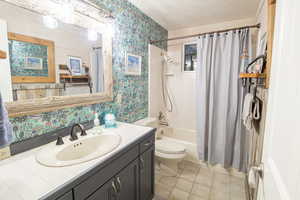 Full bathroom with wallpapered walls, a textured ceiling, shower / bath combo with shower curtain, vanity, and light tile patterned flooring