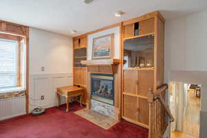 Carpeted living area featuring wainscoting, a fireplace with flush hearth, a textured ceiling, a decorative wall, and built in features