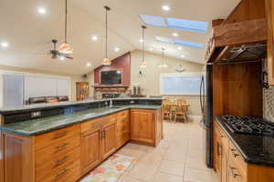 Kitchen featuring brown cabinetry, dark stone countertops, decorative light fixtures, a skylight, and custom exhaust hood