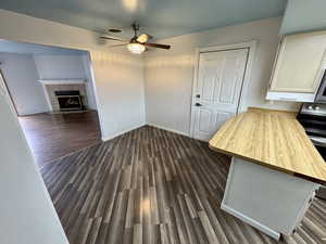 Unfurnished dining area with dark wood-type flooring, ceiling fan, and a fireplace