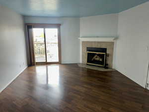 Unfurnished living room with a tiled fireplace, dark wood-style flooring, and a textured ceiling