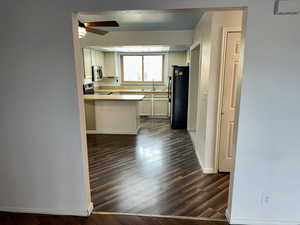 Kitchen with light countertops, stainless steel appliances, dark wood-style floors, white cabinetry, and a peninsula