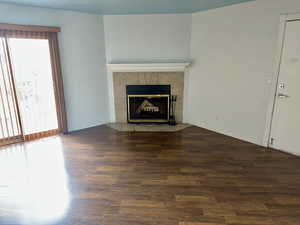 Unfurnished living room with dark wood-style flooring and a tiled fireplace