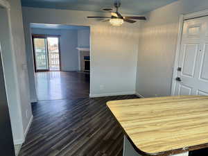 Unfurnished dining area with dark wood-style floors, ceiling fan, and a tiled fireplace