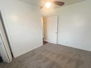 Unfurnished bedroom with dark carpet and ceiling fan
