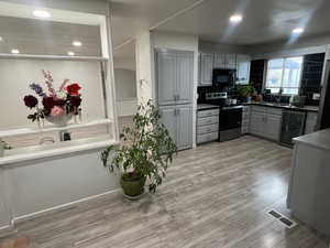 Kitchen with gray cabinets, electric stove, light wood-style floors, wine cooler, and recessed lighting