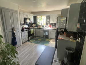 Kitchen with stainless steel appliances, light wood-style floors, wine cooler, gray cabinets, and backsplash