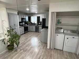 Kitchen with gray cabinets, appliances with stainless steel finishes, wine cooler, independent washer and dryer, and light wood finished floors