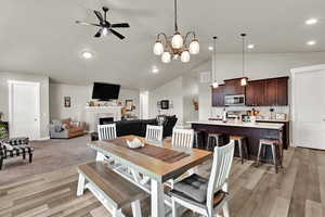 Dining space with ceiling fan, a fireplace, light wood finished floors, a chandelier, and recessed lighting