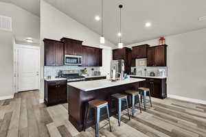 Kitchen with pendant lighting, a kitchen breakfast bar, tasteful backsplash, an island with sink, and stainless steel appliances