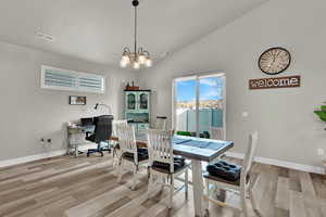 Dining space with an office area, light wood finished floors, a chandelier, and high vaulted ceiling