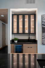 Indoor wet bar with glass insert cabinets, beverage cooler, black electric stovetop, and dark stone countertops
