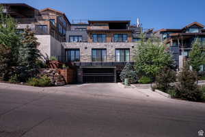 View of front facade with stone siding, concrete driveway, an attached garage, and a balcony