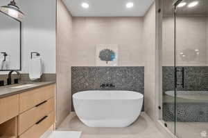 Full bathroom with tile walls, a freestanding bath, a stall shower, vanity, and recessed lighting